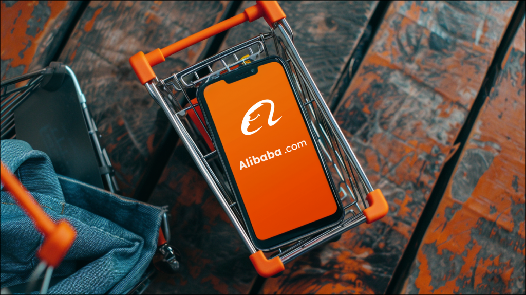 Ein Smartphone mit dem Bildschirm, der das Alibaba-Logo zeigt, liegt in einem Miniatur-Einkaufswagen 