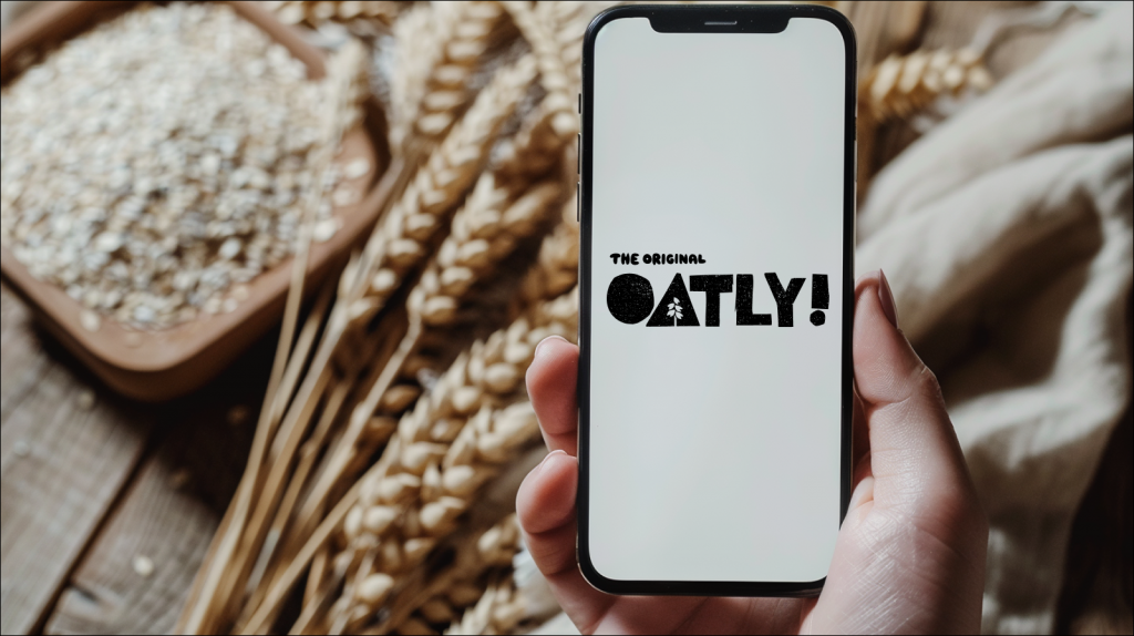 Smartphone mit weißem Bildschirm in der Hand, Haferflocken und Oatly im Hintergrund