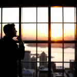 Nachdenklicher Investor am Fenster bei Sonnenuntergang