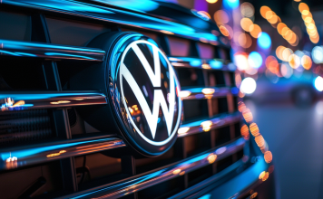 Nahaufnahme des Volkswagen-Logos am Kühlergrill eines neuen, glänzenden SUVs mit reflektierenden Stadtlichtern